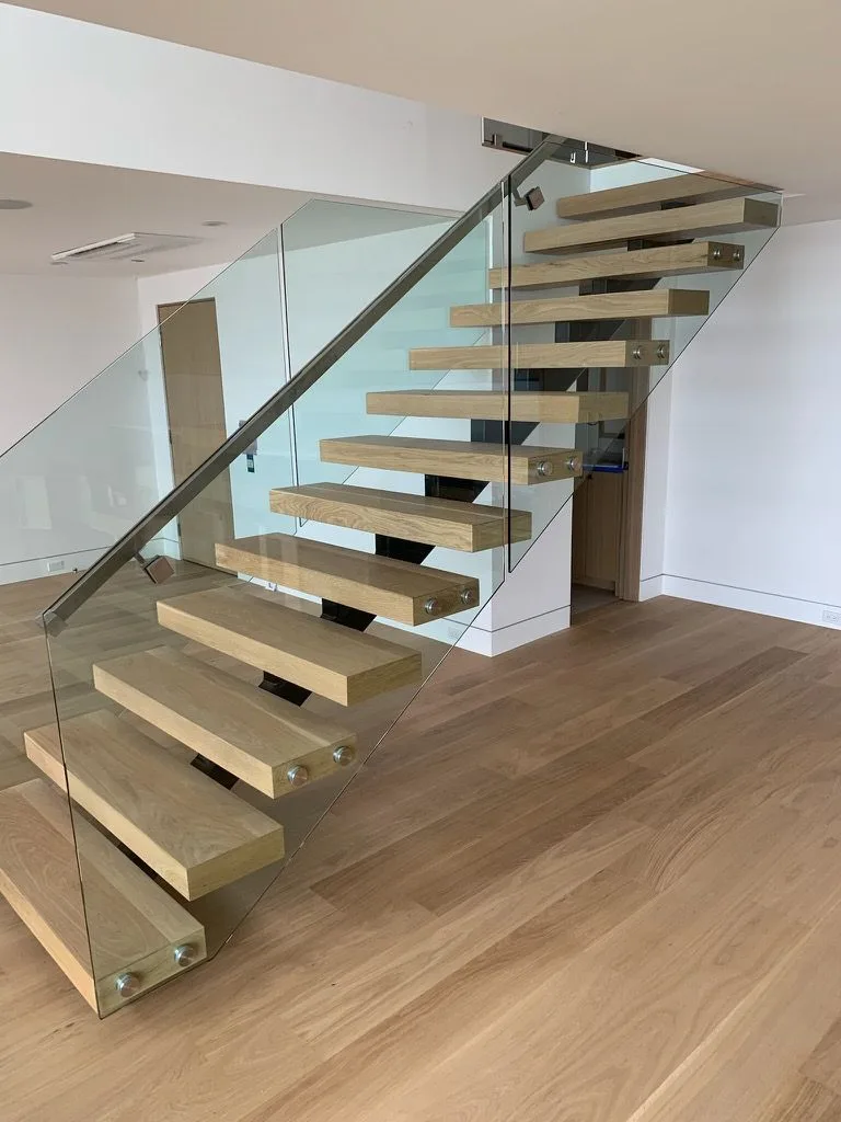 Floating white oak treads on a single steel stringer behind a glass rail, wide-plank oak below in Redondo Beach