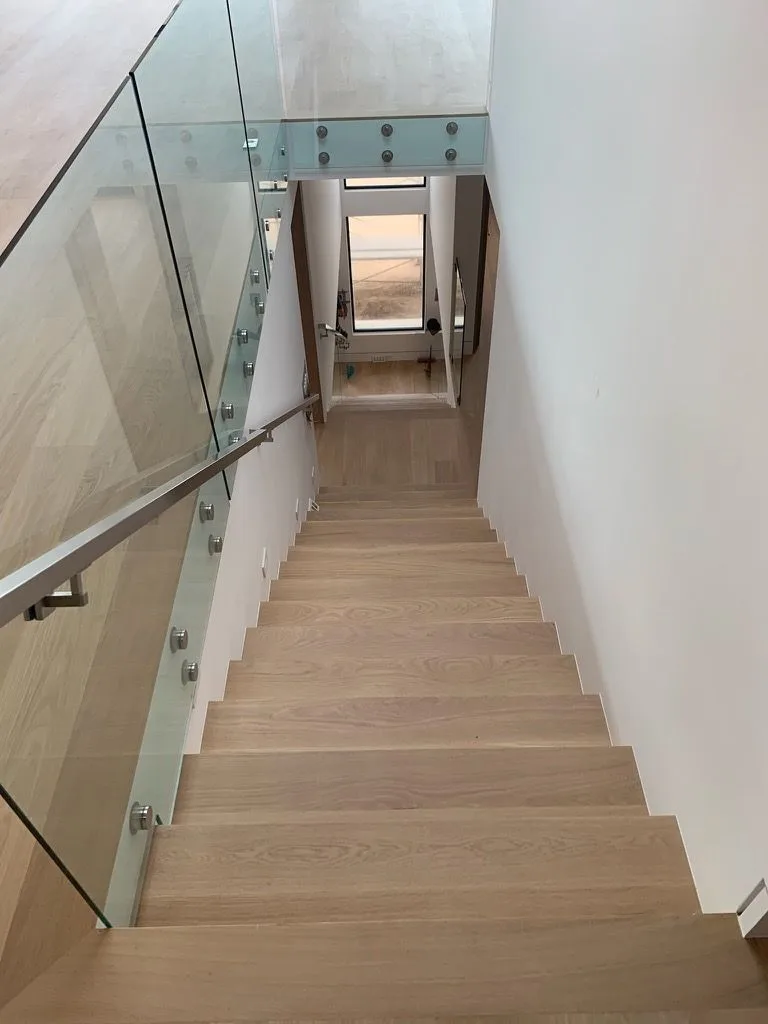 Looking down a straight run of white oak stairs between glass panels in Redondo Beach