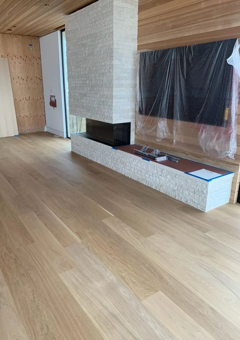 White oak planks past a stacked-stone fireplace, protection still on the windows in Redondo Beach