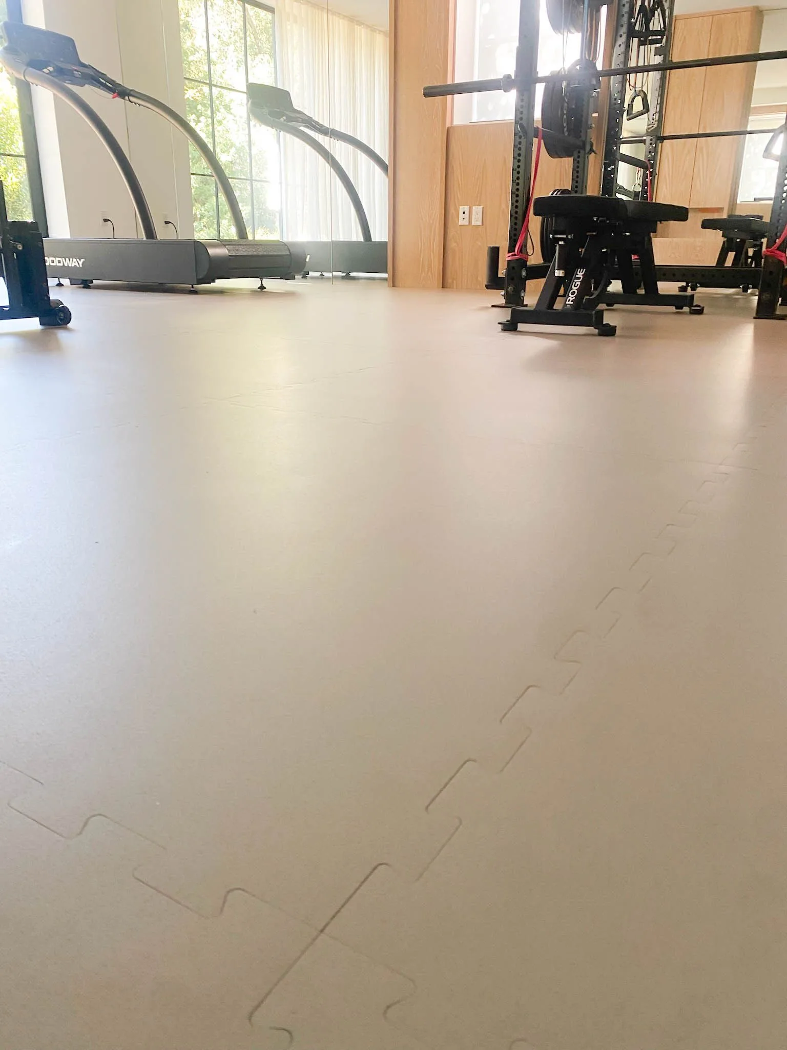 Interlocking rubber gym tiles seamed tight, treadmills along the window