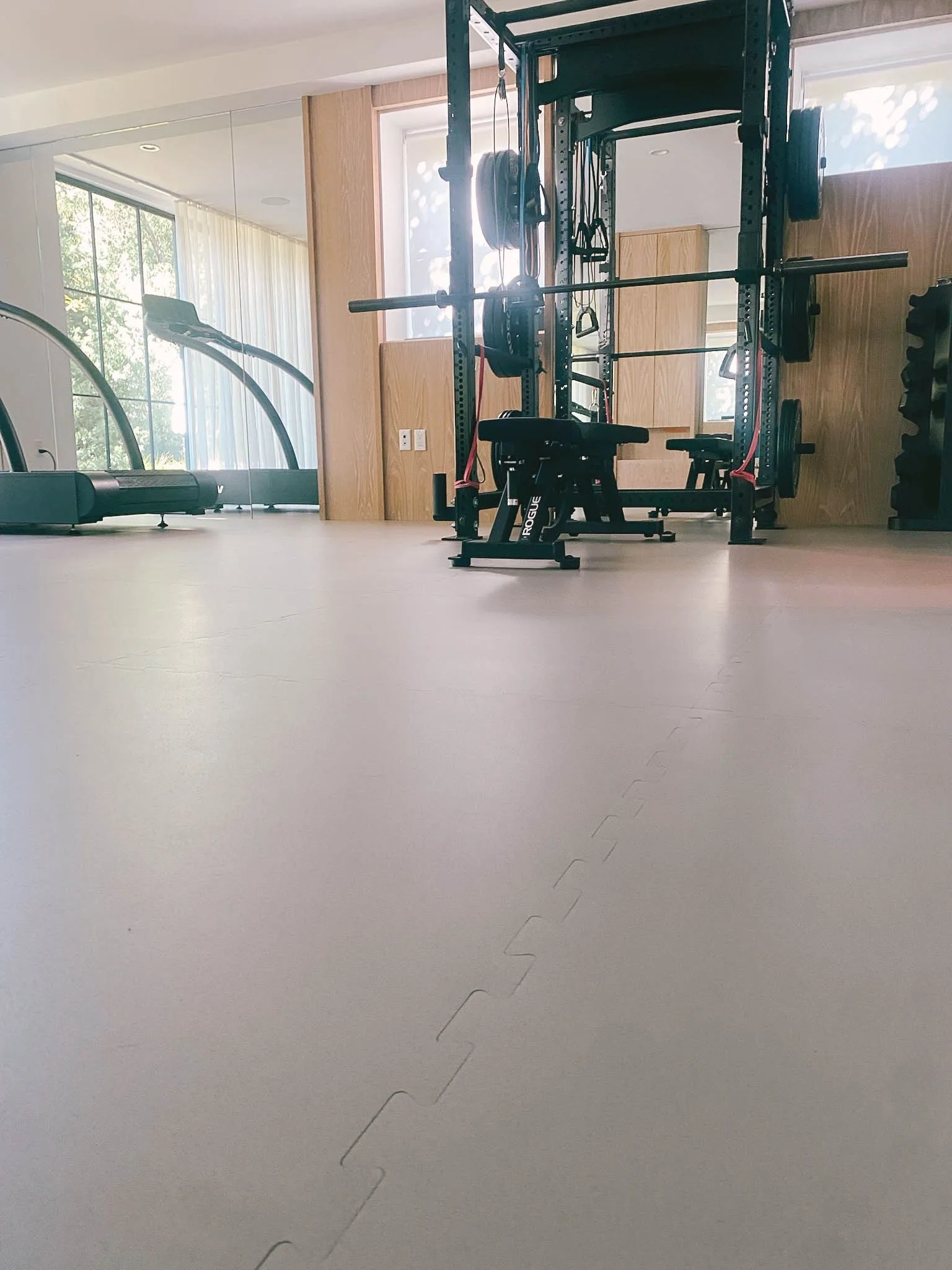 Low view across grey rubber gym flooring to a squat rack and weight bench
