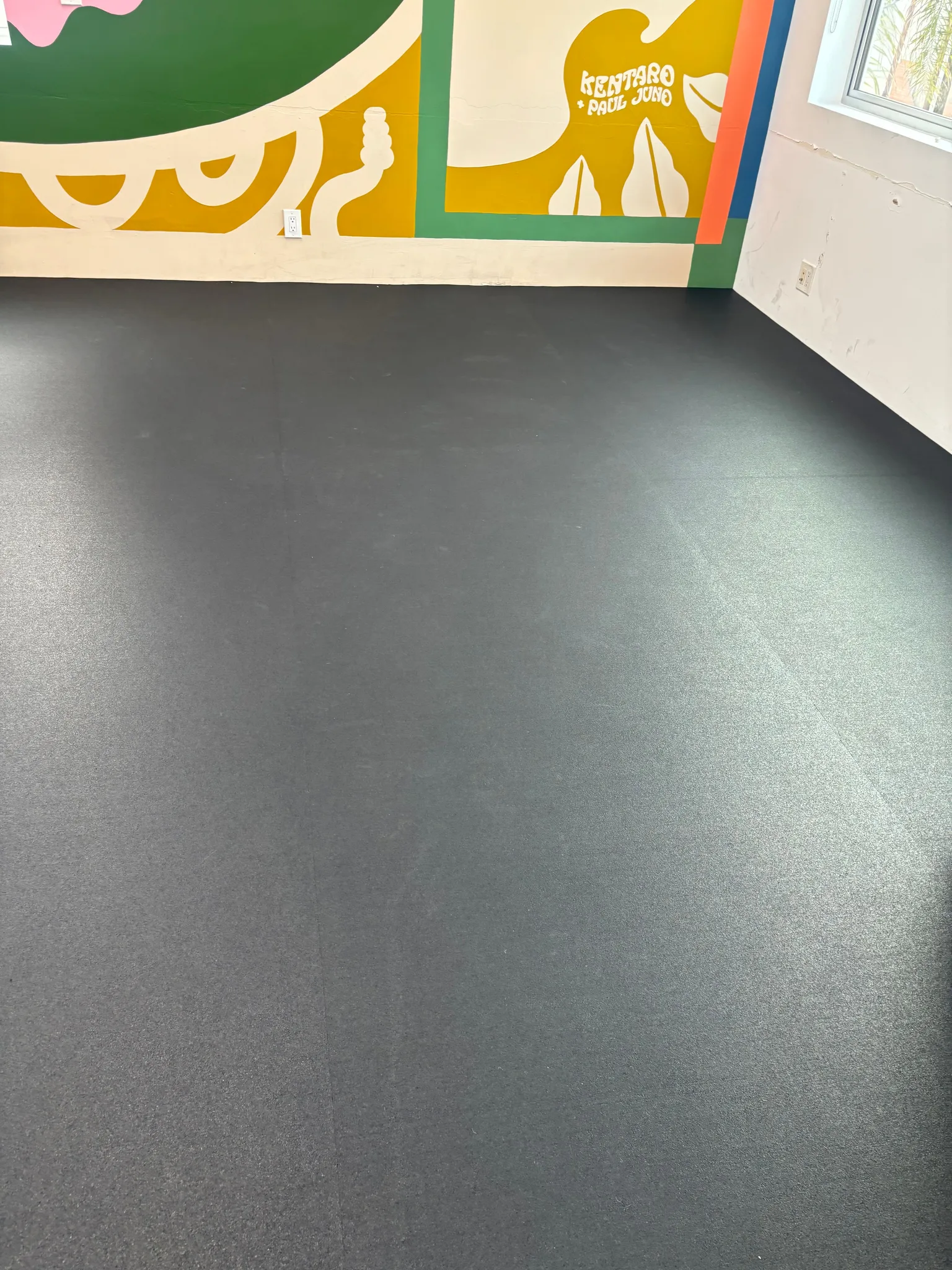 Black rubber gym floor laid wall to wall in a studio with a painted mural