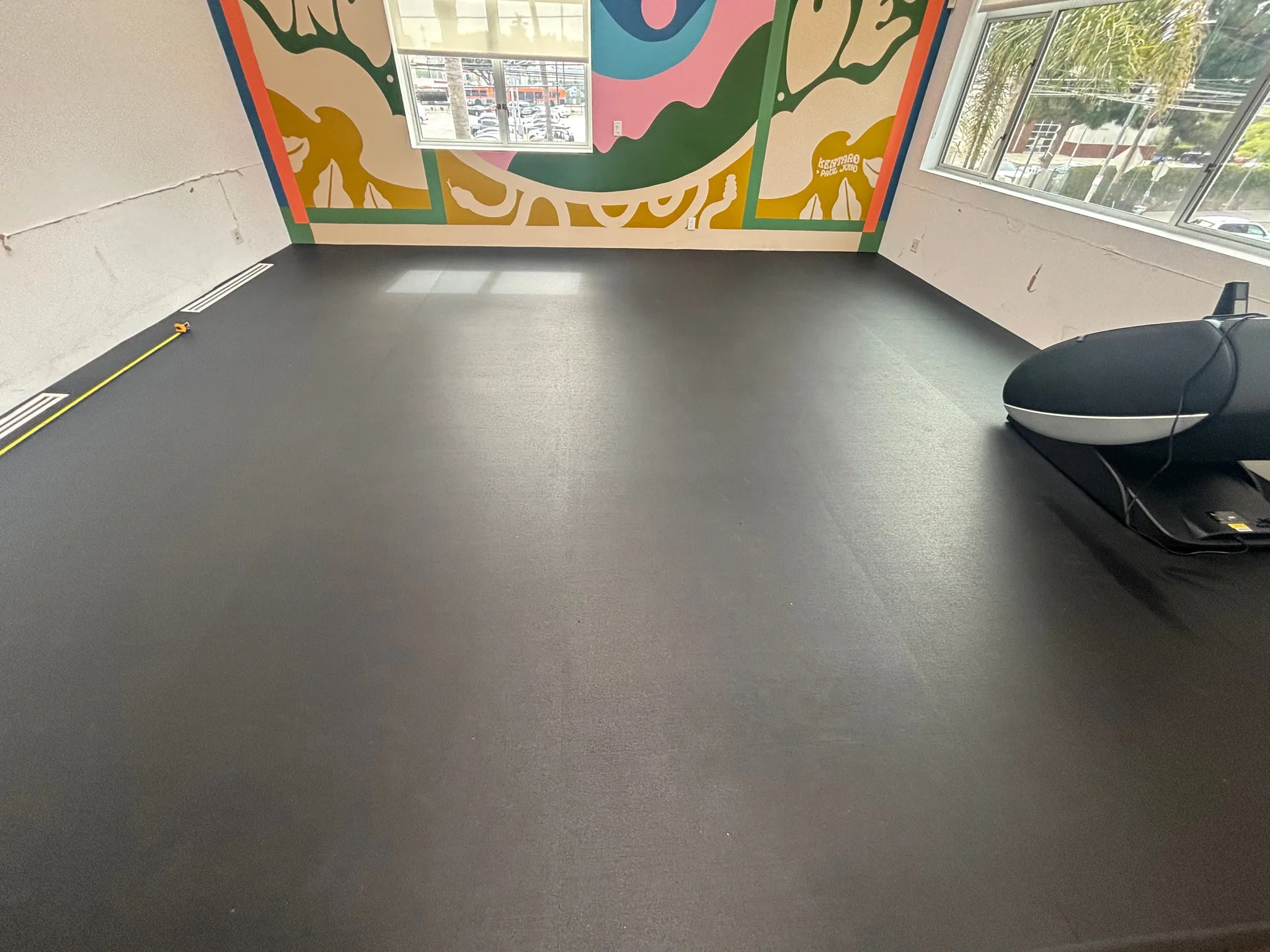 Black rubber flooring across a studio with a mural and street-facing windows