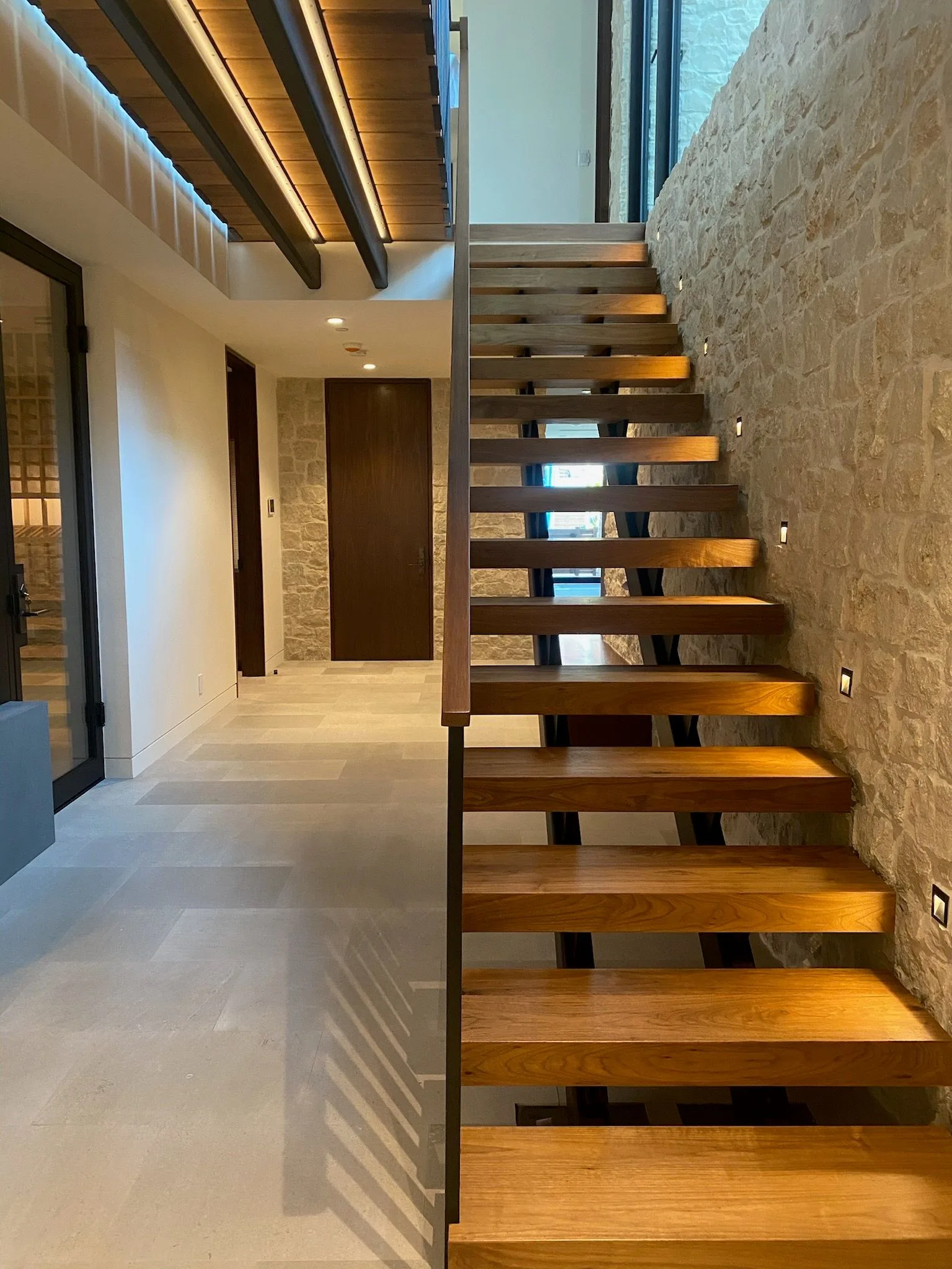 Open-riser walnut stair between stone and glass in Hermosa Beach