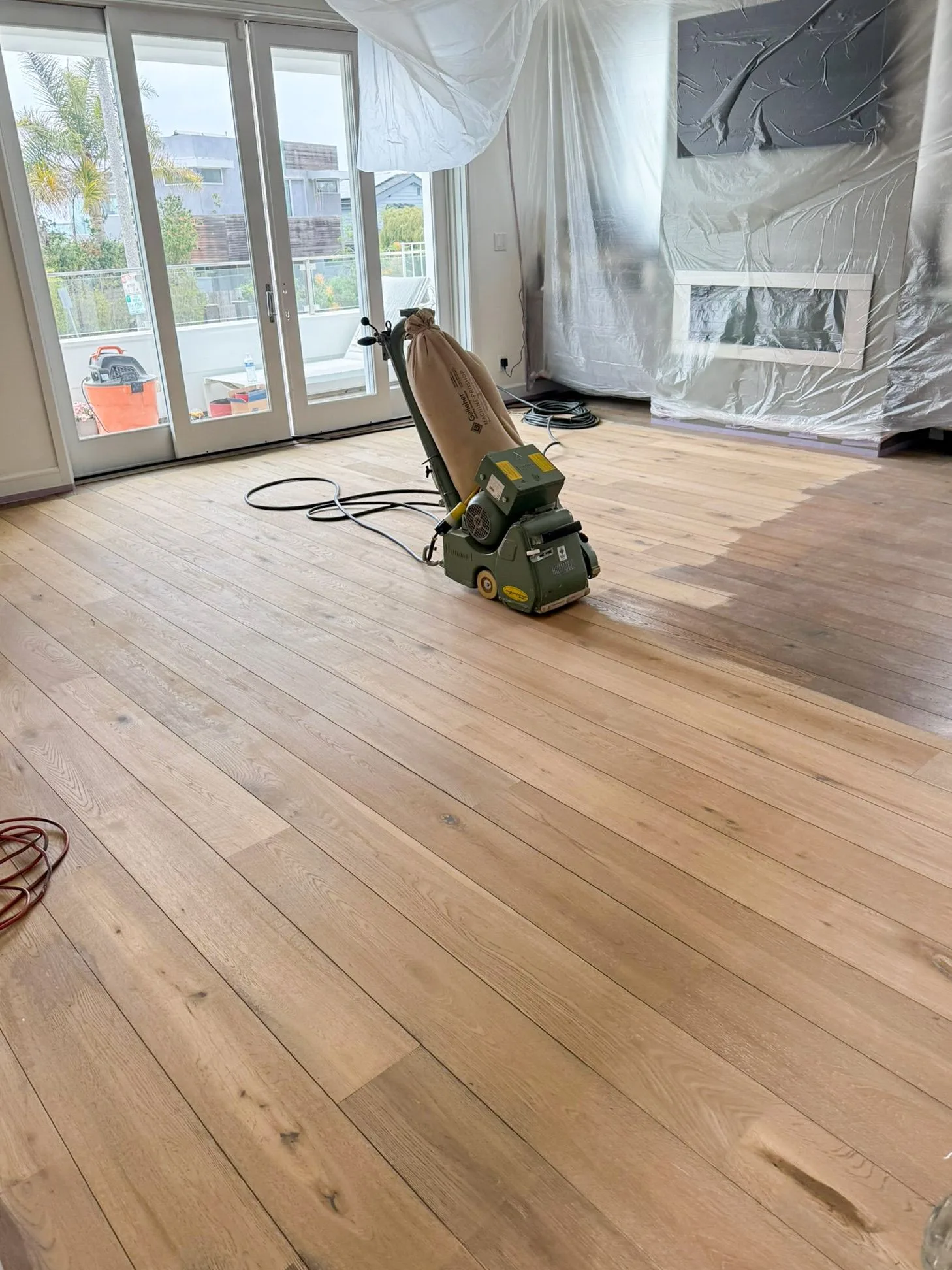 Drum sander mid-pass on a wide-plank oak floor