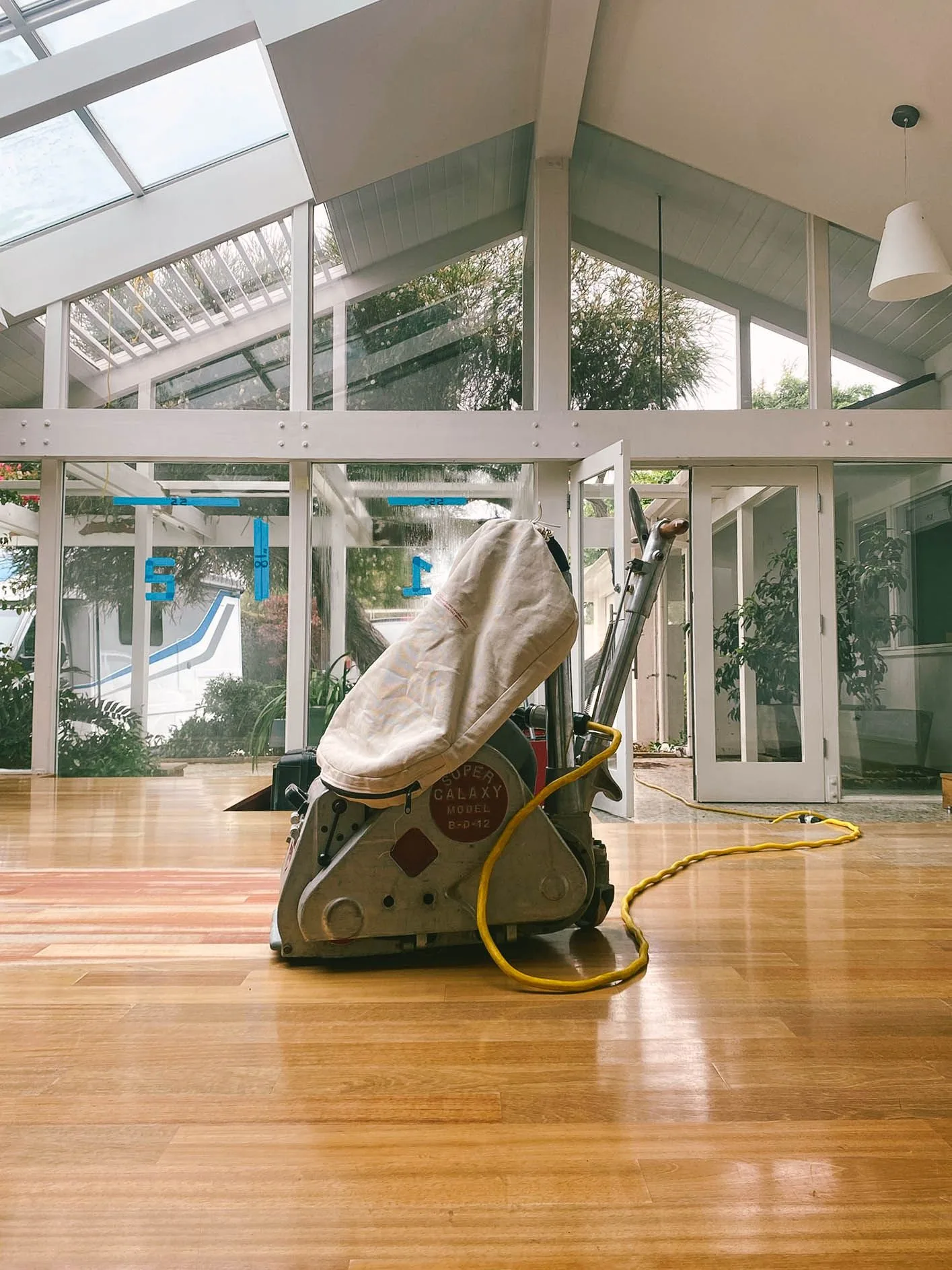 Drum sander staged on a strip floor in a glass-walled room