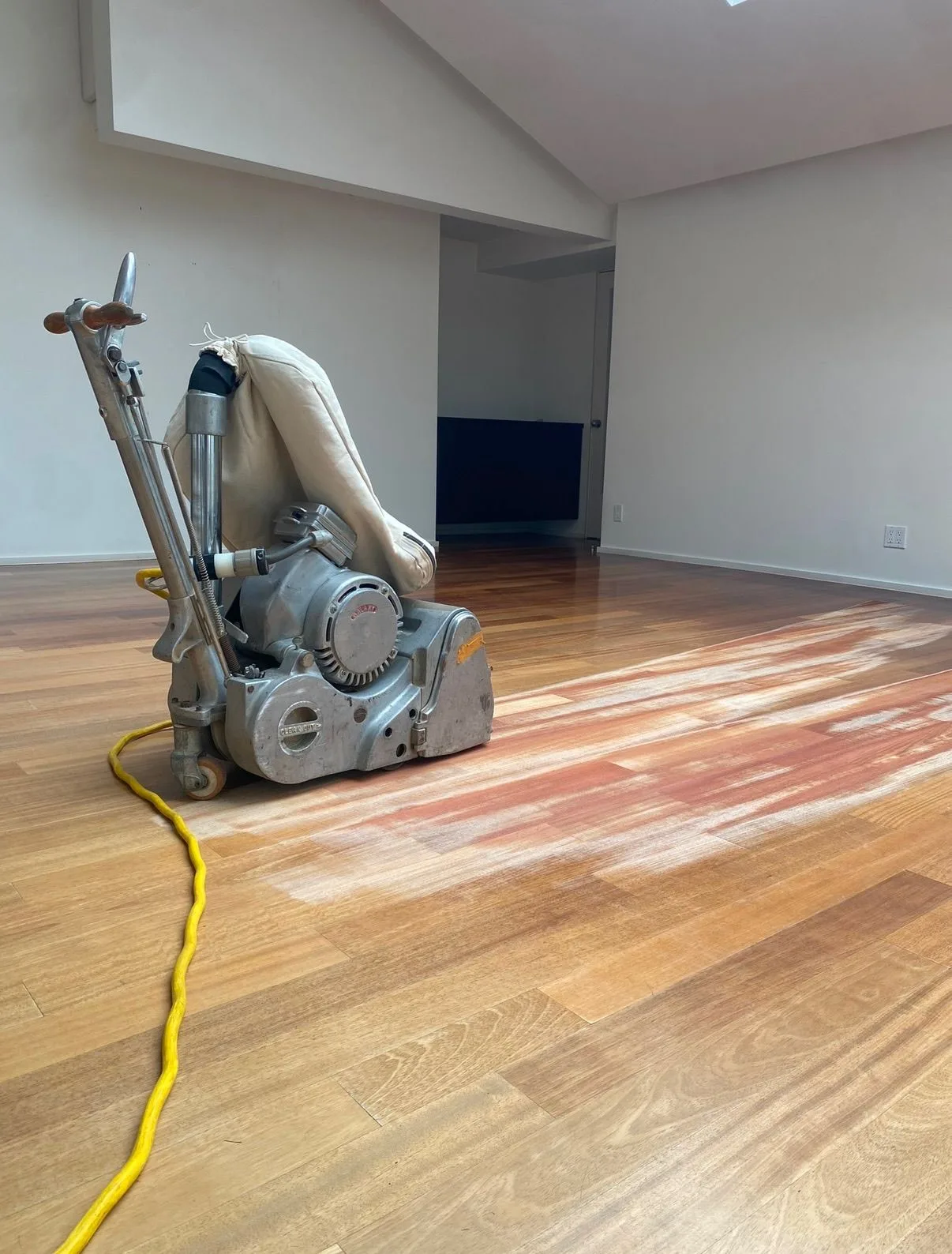 Red-toned hardwood showing through the first sanding pass