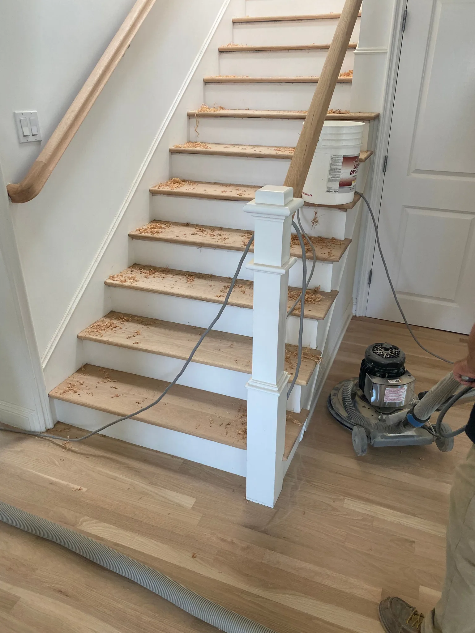 Stair treads scraped and sanded during a refinish, buffer on the floor below
