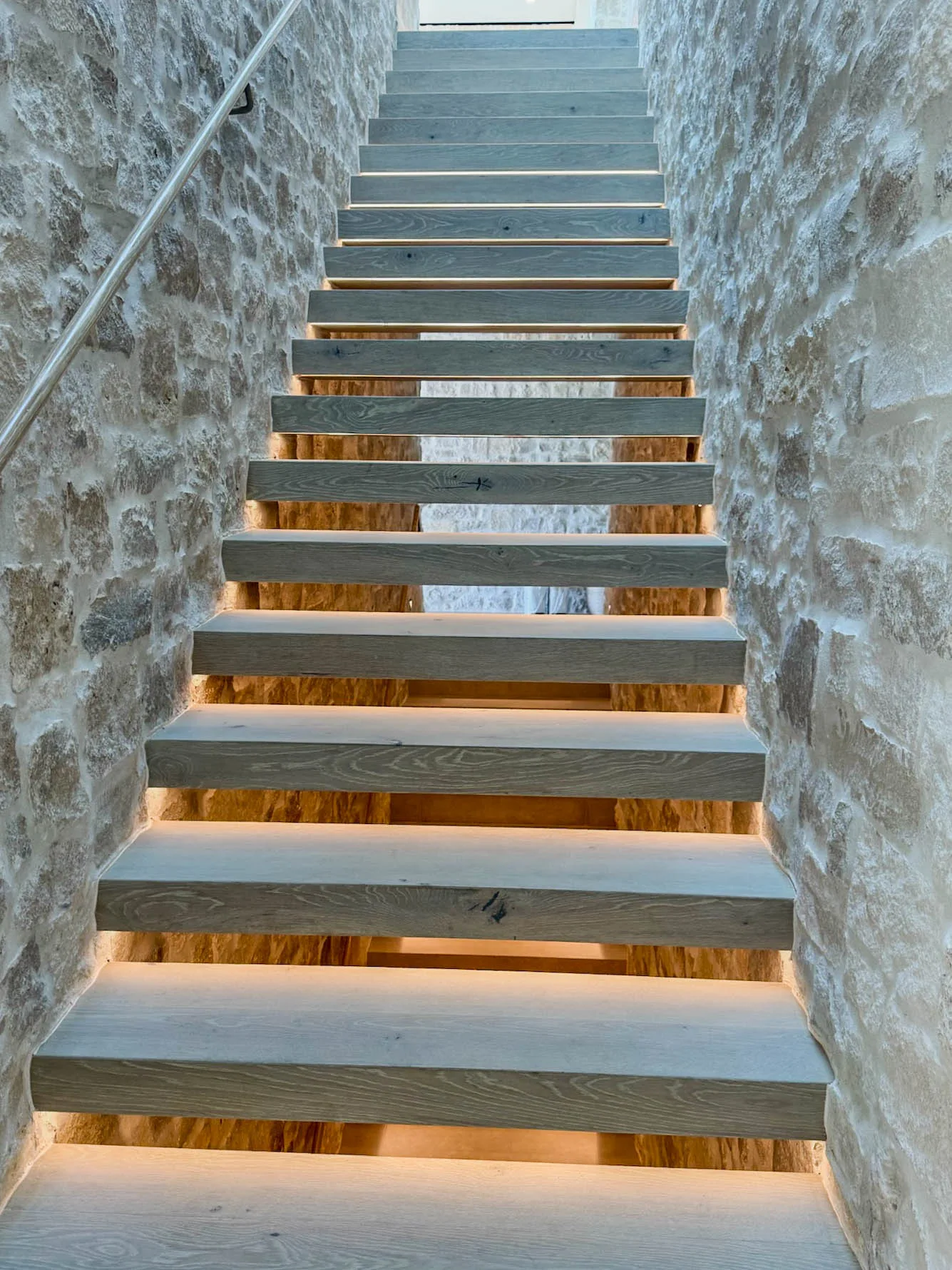 Floating treads with under lit LED strip lighting between stone walls in Manhattan Beach
