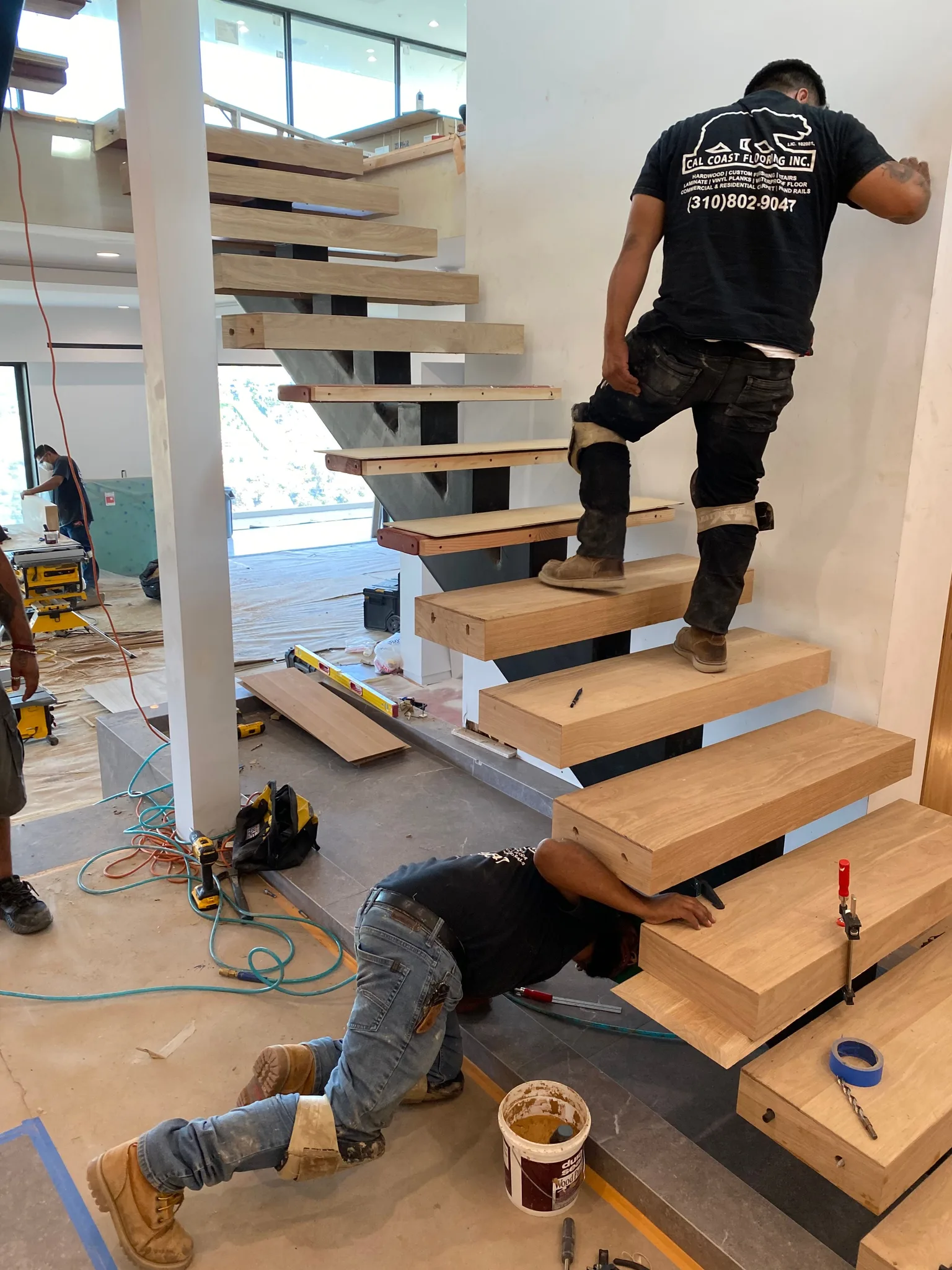 Cal Coast Flooring crew fastening thick oak treads to a steel-stringer floating stair