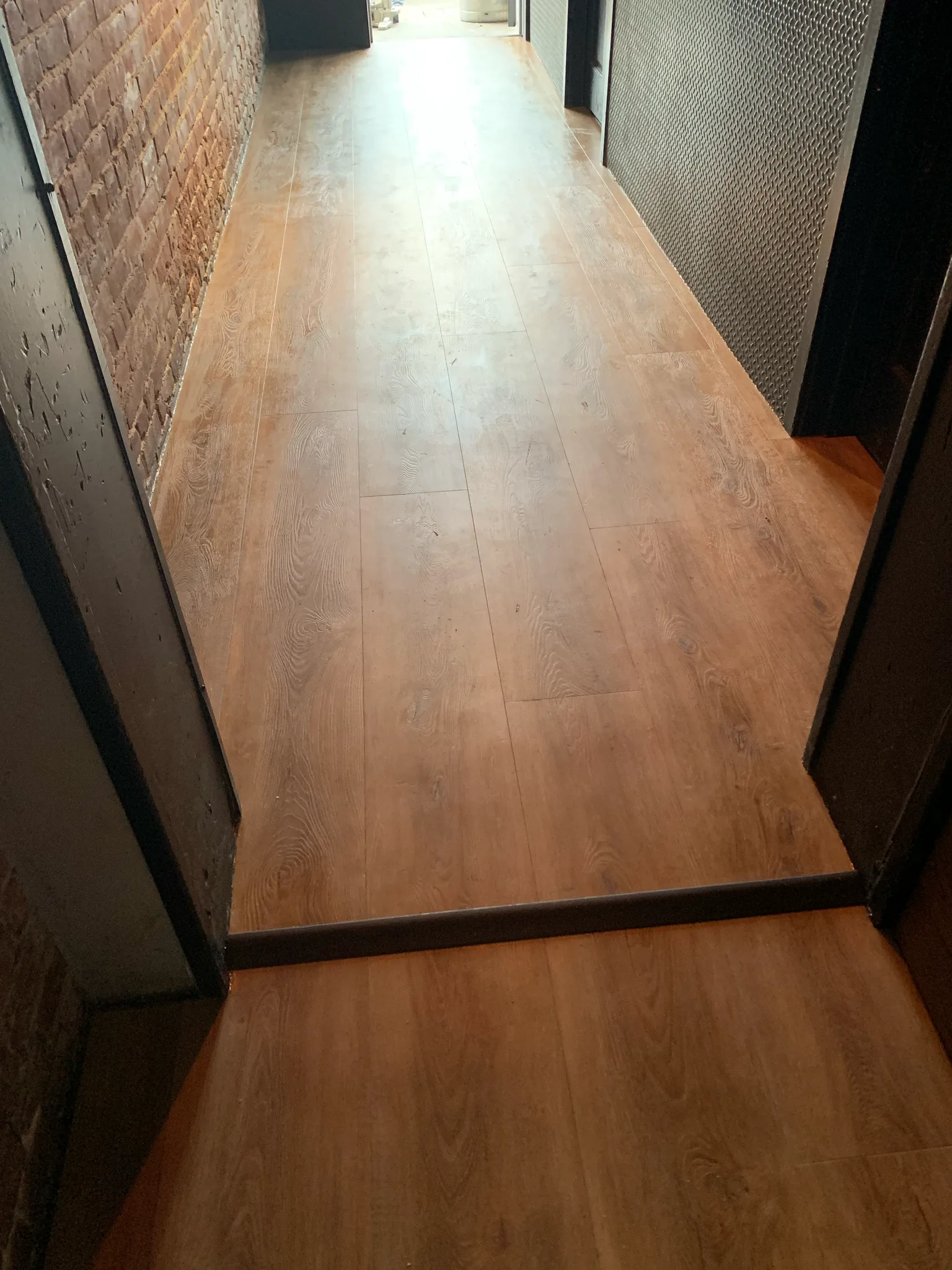 Luxury vinyl plank flooring with a dark transition strip in a corridor at American Junkie — Cal Coast Flooring