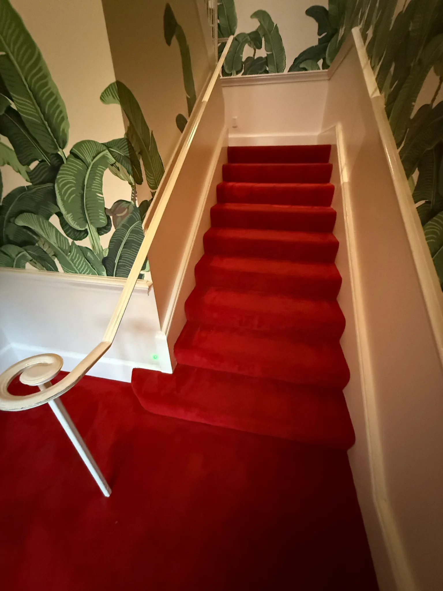 New red carpet on the grand staircase beside banana-leaf wallpaper at The Beverly Hills Hotel