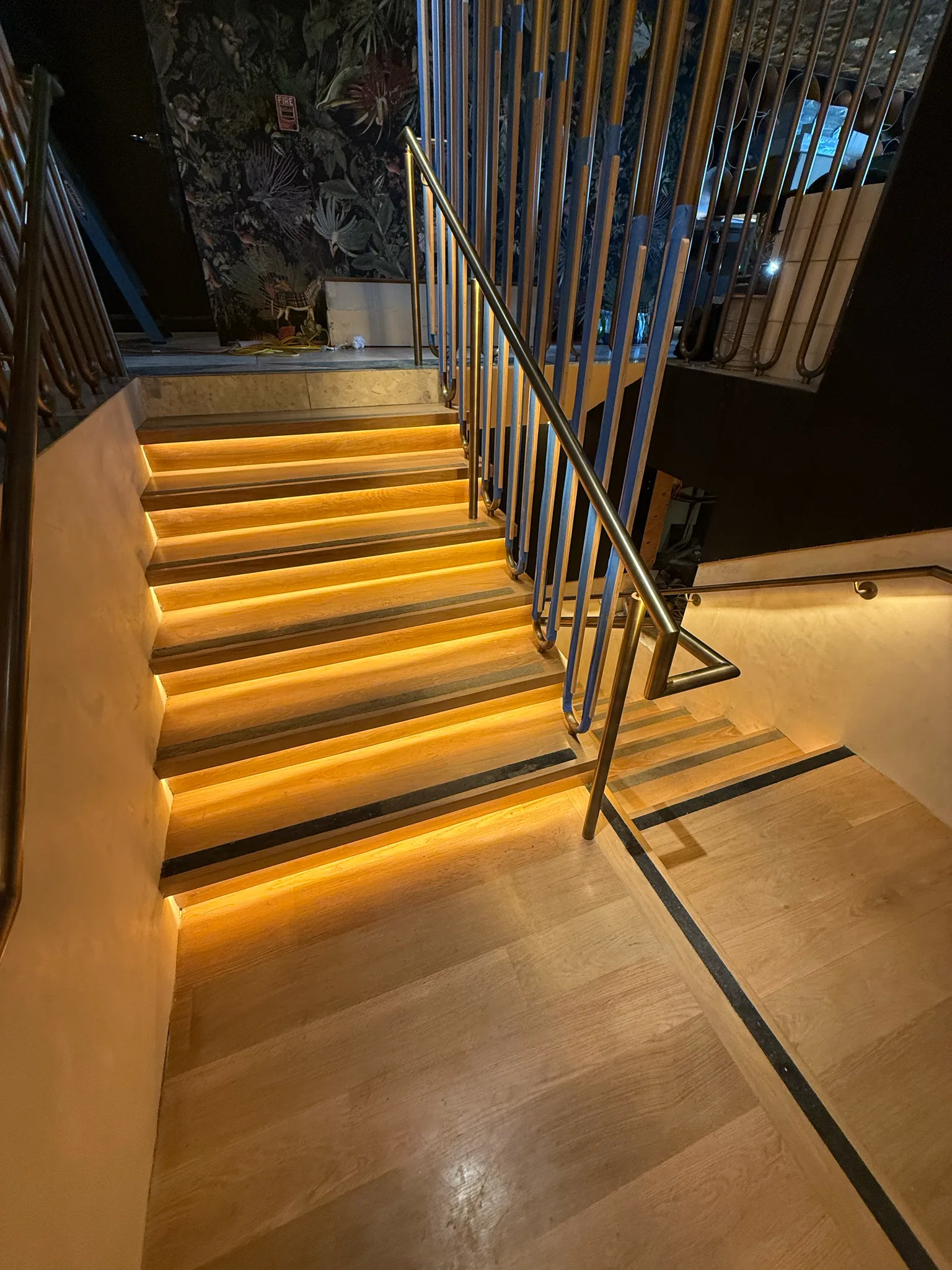 Finished wood staircase with LED-lit treads and brass railings, built by Cal Coast Flooring at Esperanza