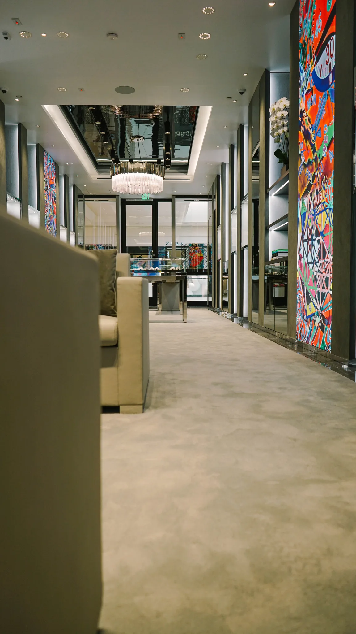 Low view along the grey carpet beside a colorful art panel and mirrored columns at Hublot