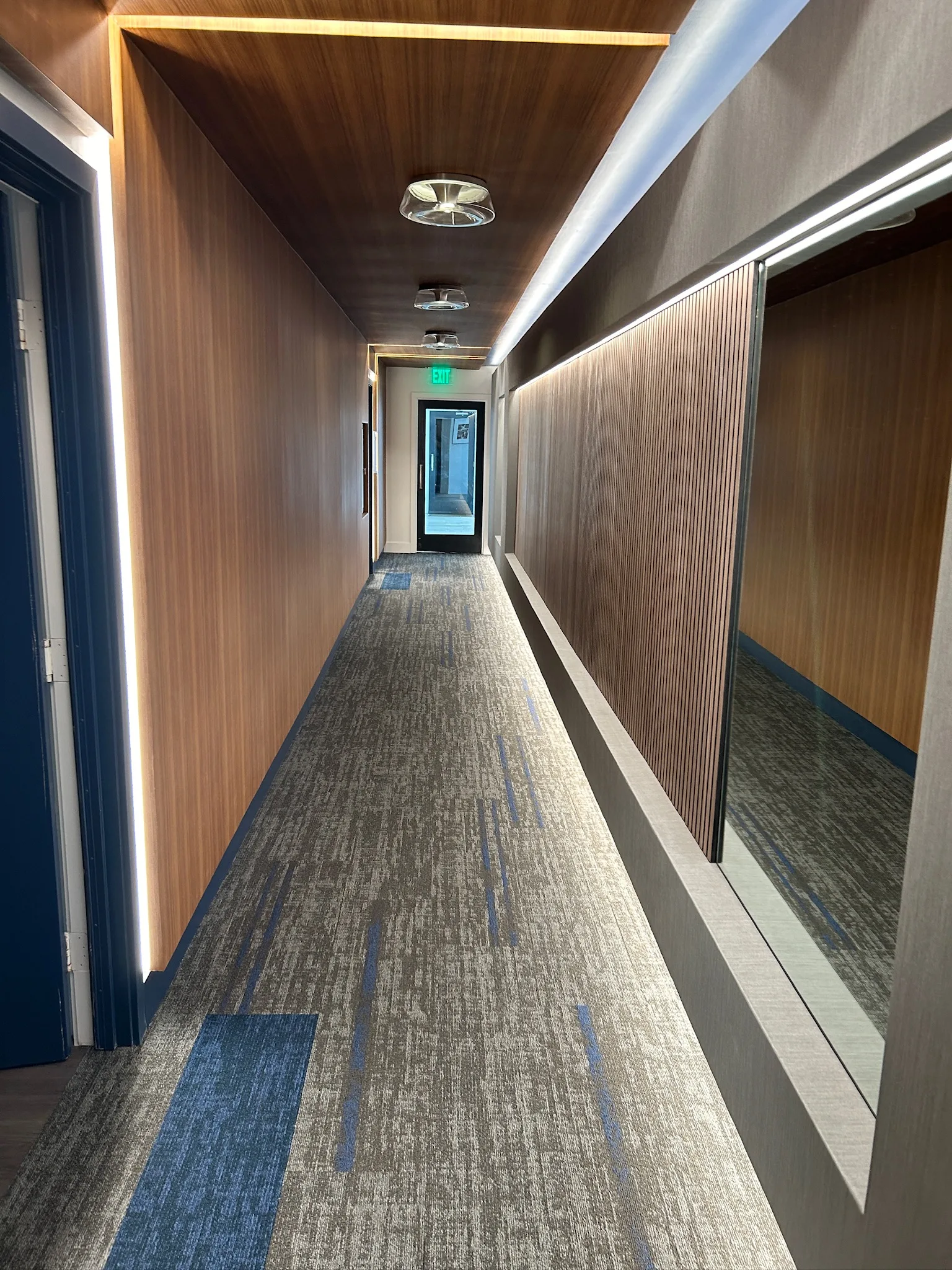 Patterned gray-and-blue carpet tile down a wood-panelled guest corridor at the Sunset Marquis
