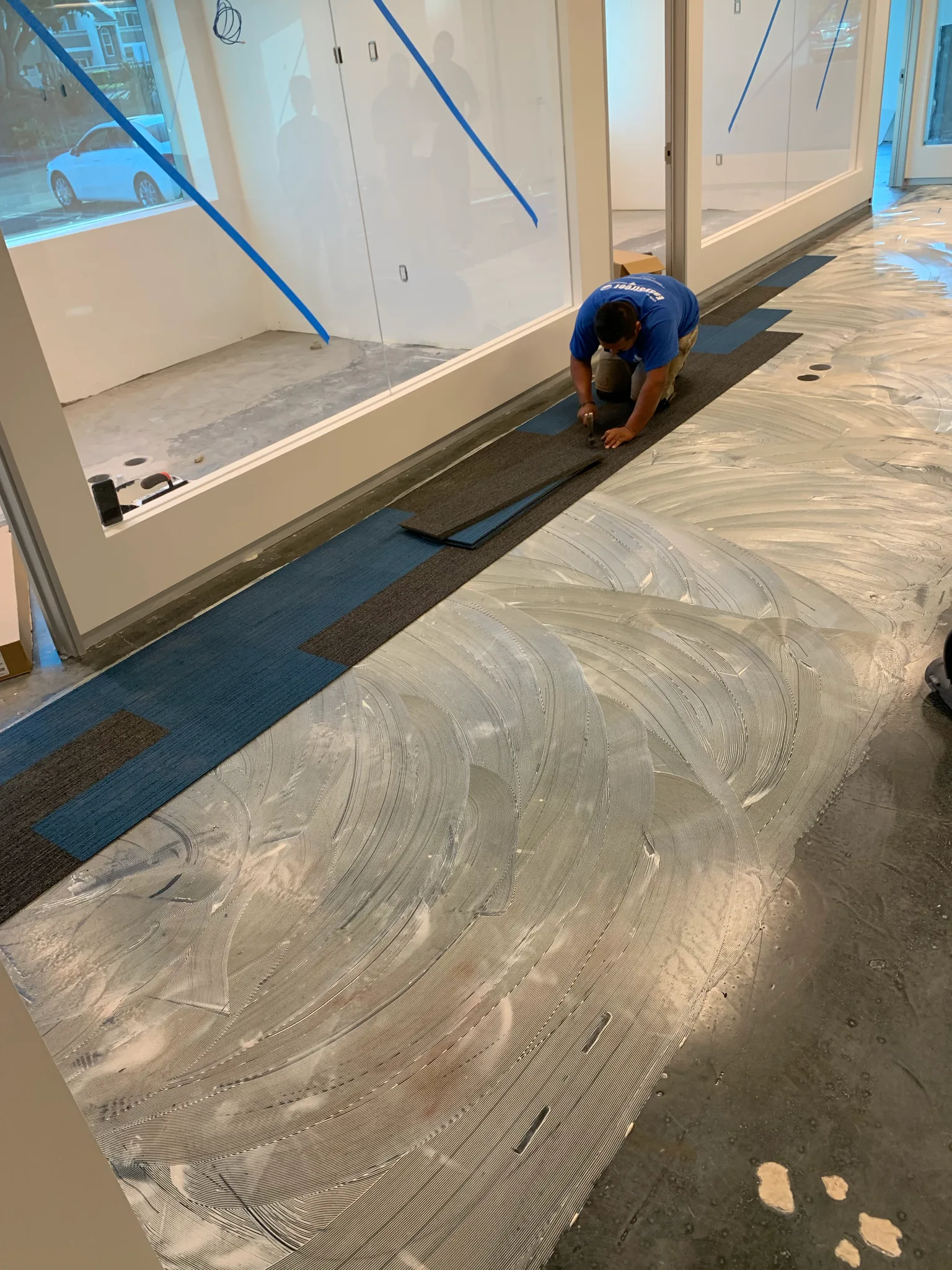 Blue and charcoal carpet tile going down over the cured moisture barrier along glass-walled offices at Wedgewood