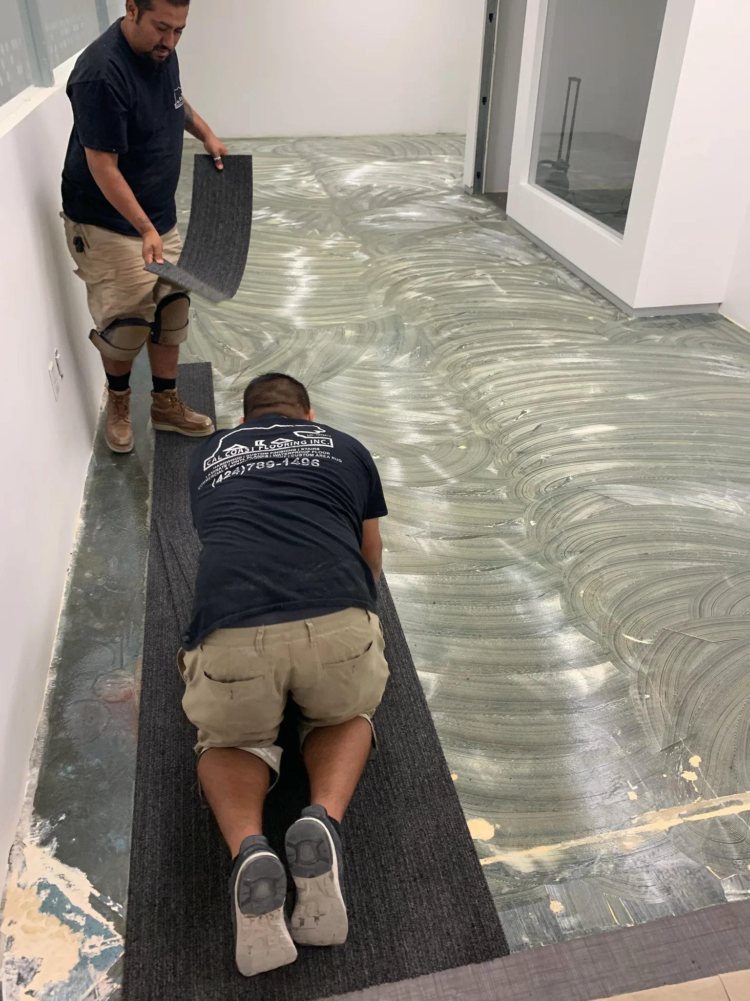 Carpet tile being set over the moisture barrier in a Wedgewood office, Cal Coast Flooring crew at work