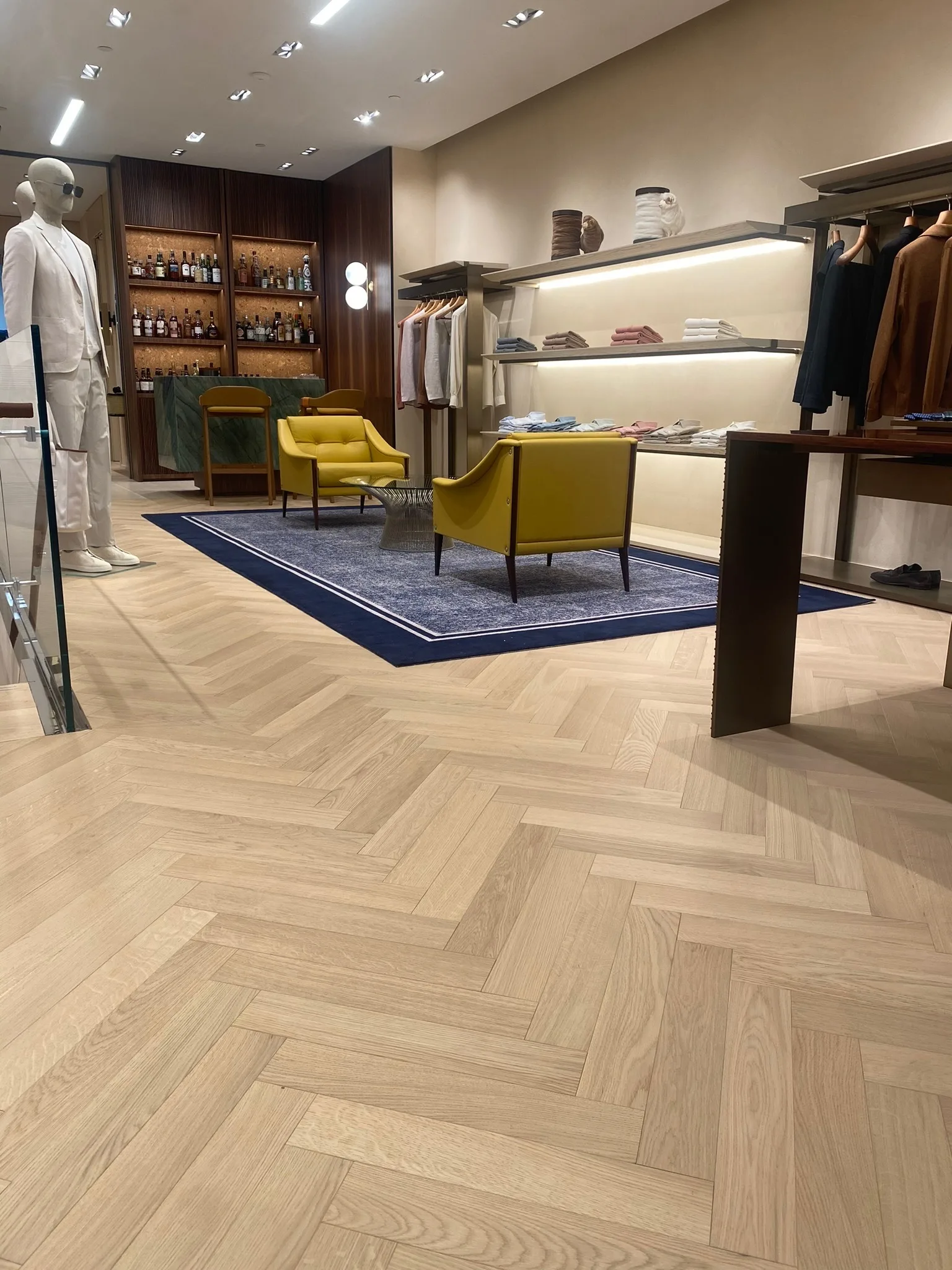 Light oak herringbone floor framing a lounge with yellow armchairs at Zegna Beverly Hills