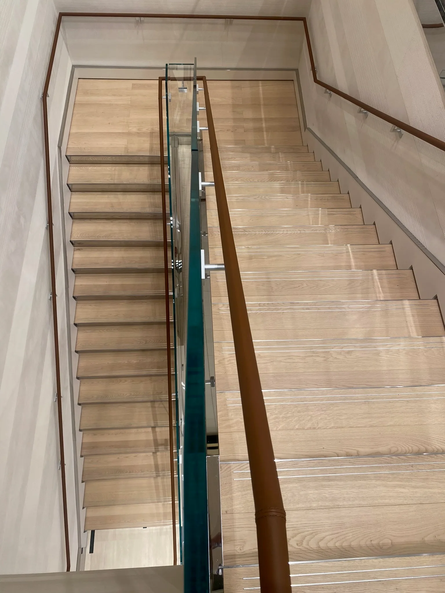 Prefinished oak steps with custom metal trim beside the glass railing at Zegna Beverly Hills, seen from above